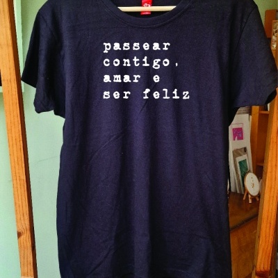 T-shirt preta com texto branco pendurada em cabide de madeira
