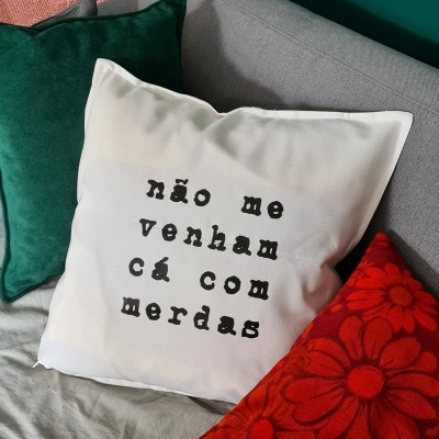 Três almofadas coloridas com texto em sofá cinzento contra parede verde