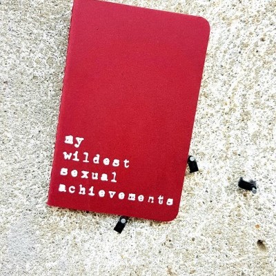 Caderno vermelho com texto branco sobre superfície de cimento