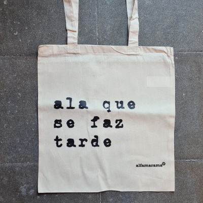 Mala de tecido cru com texto impresso a preto sobre chão cinzento