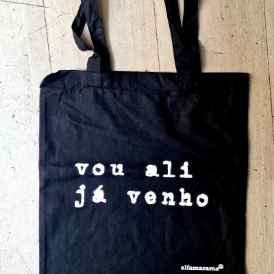 Mala de pano preta com texto branco vou ali já venho