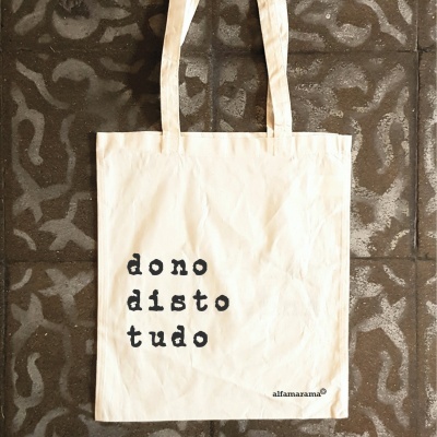 Saco de pano branco com texto preto pendurado contra chão de azulejos castanhos
