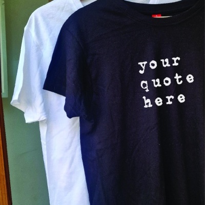 T-shirts preta com texto e branca penduradas em cabides de madeira