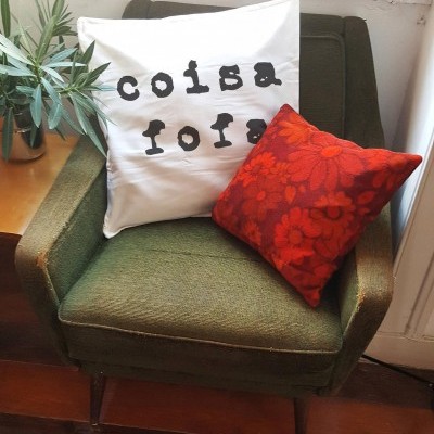 Poltrona verde com duas almofadas e planta em mesa ao lado