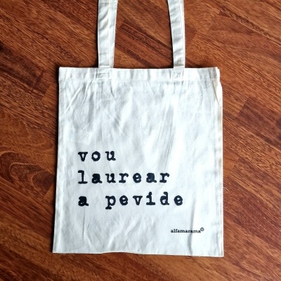 Saco de tecido branco com texto em preto sobre chão de madeira