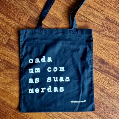 Saco de tecido preto com texto branco sobre chão de madeira