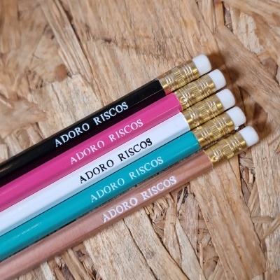 Cinco lápis coloridos com texto ADORO RISCOS numa superfície de madeira