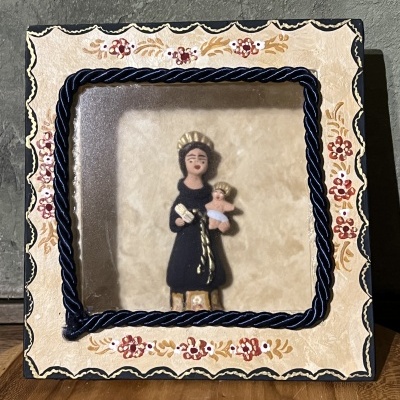 Quadro religioso decorativo com moldura floral e figura de mulher e criança em relevo.