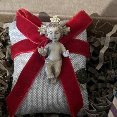 Almofada cinza com fita vermelha de veludo e anjo cerâmico dourado num fundo de papel rasgado