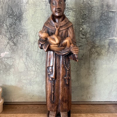 Estátua em madeira de santo com criança nos braços sobre superfície de madeira