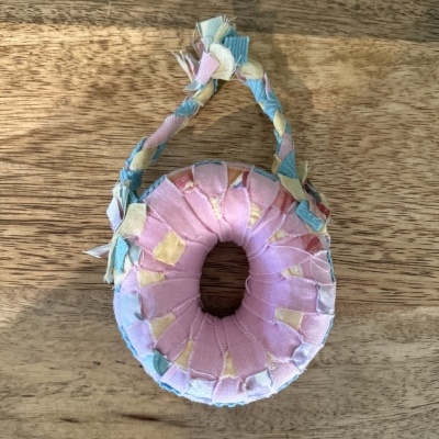 Chaveiro artesanal de tecido rosa, azul e amarelo com alça torcida sobre madeira clara