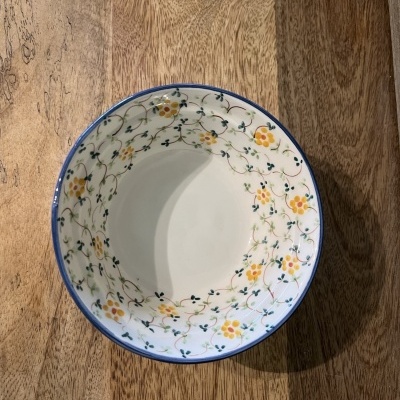 Taça branca com padrão floral amarelo e verde embutida numa mesa de madeira clara