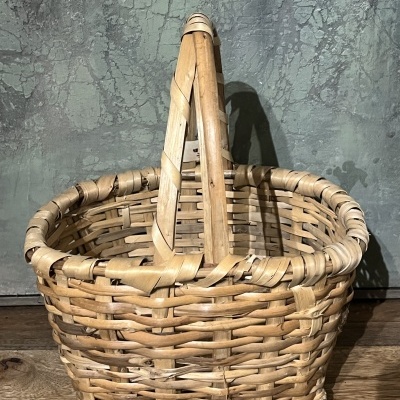 Cesto trançado de verga natural com alça dupla sobre piso de madeira