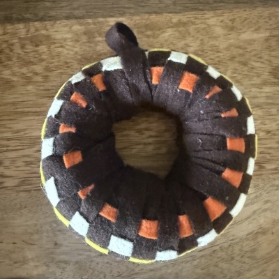 Elástico de cabelo de tecido felpudo castanho com padrão laranja, branco e amarelo sobre madeira