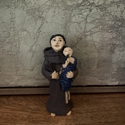 Estatueta de homem com criança em hábito castanho e pano azul sobre superfície de madeira