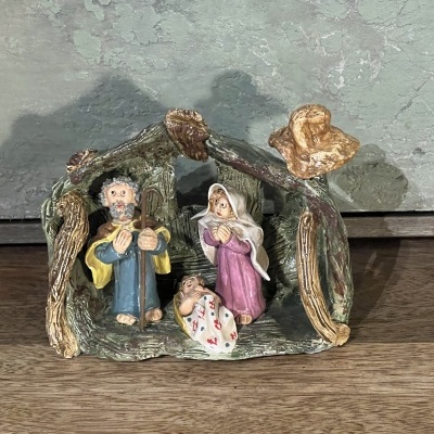 Presépio pequeno decorativo com figuras de José, Maria e Menino Jesus em estrutura que parece madeira.