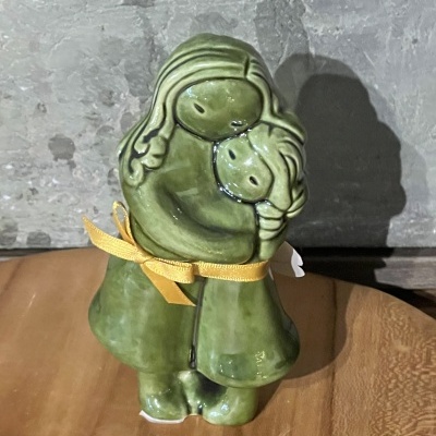 Escultura cerâmica verde de duas figuras a abraçarem-se com laço amarelo colocada sobre madeira