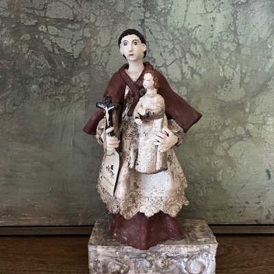 Estátua religiosa de santo com crucifixo e figura, sobre base ornamentada