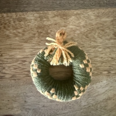 Miniatura de guirlanda decorativa de lã verde e amarela com laço, sobre mesa de madeira