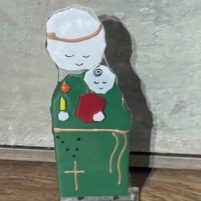 Estátua de monge em hábito verde segurando uma criança, com detalhes dourados