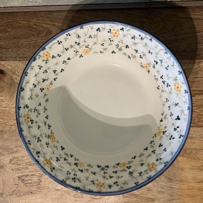 Prato fundo branco com padrão floral azul e amarelo na borda sobre mesa de madeira