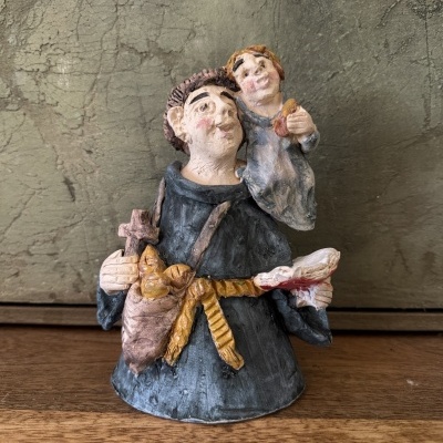 Estatueta cerâmica de frade com criança ao colo em hábito azul e cinto amarelo