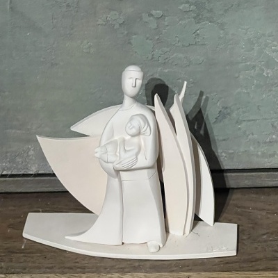 Escultura de cerâmica branca de figura humana segurando bebê com formas abstratas atrás.