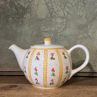 Chaleira de cerâmica branca com padrão floral vermelho e verde e listas amarelas, sobre superfície de madeira