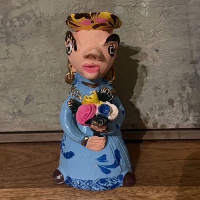 Estatueta cerâmica feminina com vestido azul e chapéu amarelo a segurar flores.