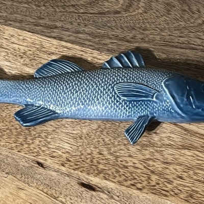 Peixe decorativo azul em metal com textura de escamas sobre madeira