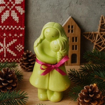 Escultura verde de cerâmica de duas figuras femininas abraçadas com laço rosa em cenário natalício