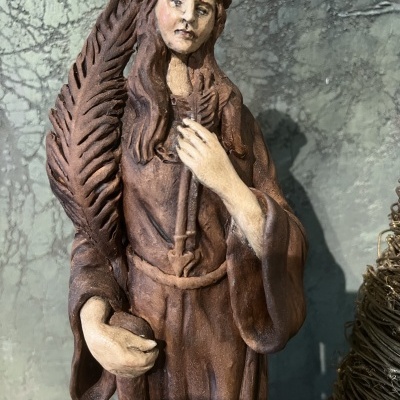 Estátua de figura feminina com roupa castanha e pena grande numa mão