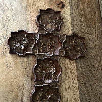 Cruz de madeira com painéis em relevo representando cenas bíblicas sobre superfície de madeira clara