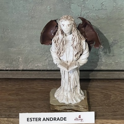 Estátua de anjo branco com asas castanhas e livro aberto
