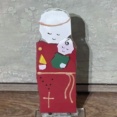 Estátua de vidro colorido de figura religiosa com criança sobre base transparente