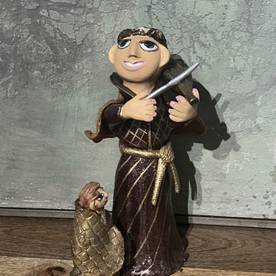 Figura de cerâmica de duas personagens, uma maior e outra menor, em cenário rústico.