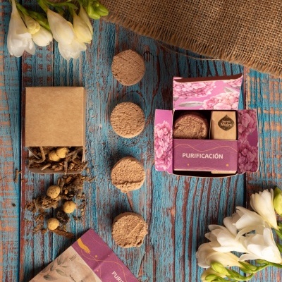 Discos esfoliantes marrons com embalagem roxa e castanha e flores brancas sobre mesa azul de madeira rústica