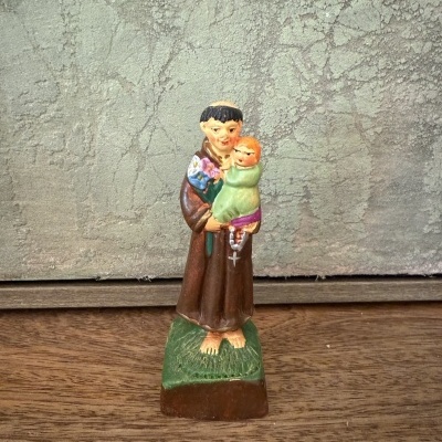 Estátua religiosa de homem com hábito castanho segurando criança em vestido verde