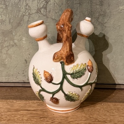 Botija de cerâmica branca decorada com ramo e folhas em relevo, duas bicas e pega imitação madeira.