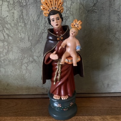 Estátua decorativa de homem com túnica vermelha segurando menino nu com coroa alaranjada