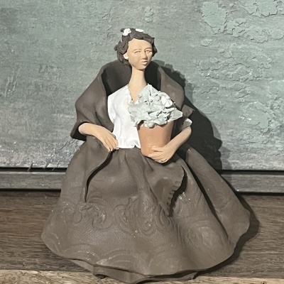 Estátua feminina com vestido castanho e flores brancas numa mão