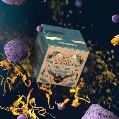 Embalagem cúbica com texto Kit Humito Sagrado rodeada por esferas roxas e pétalas amarelas