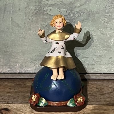 Estátua de criança com túnica branca e dourada sentada em esfera azul com flores