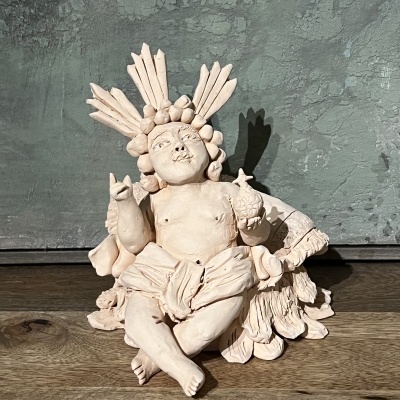 Escultura em cerâmica de figura humana com detalhes decorativos, sobre superfície de madeira