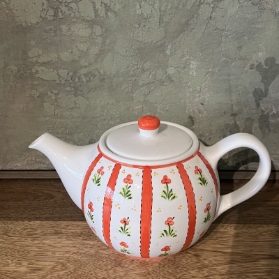 Chaleira de cerâmica branca com flores cor-de-laranja e verde sobre mesa de madeira