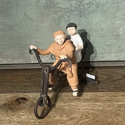 Figuras decorativas de cerâmica com duas crianças numa bicicleta em madeira sobre mesa de madeira