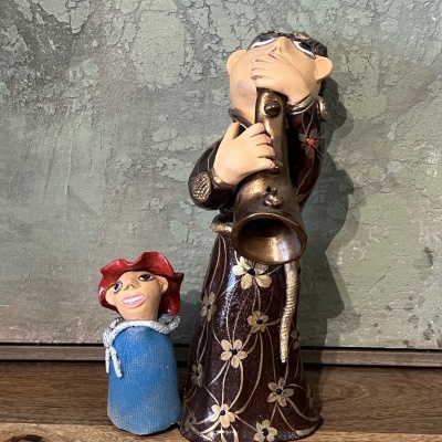 Figuras decorativas em cerâmica de músico e boneco colorido sobre uma superfície de madeira com fundo cinzento texturizado