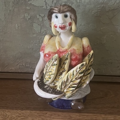 Escultura de cerâmica colorida de figura feminina segurando espigas de milho.