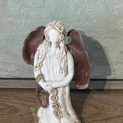 Estátua de anjo cerâmica com asas castanhas sobre base de pedra