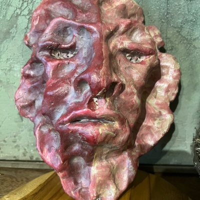 Máscara decorativa esculpida com rosto humano em tons de vermelho e rosa